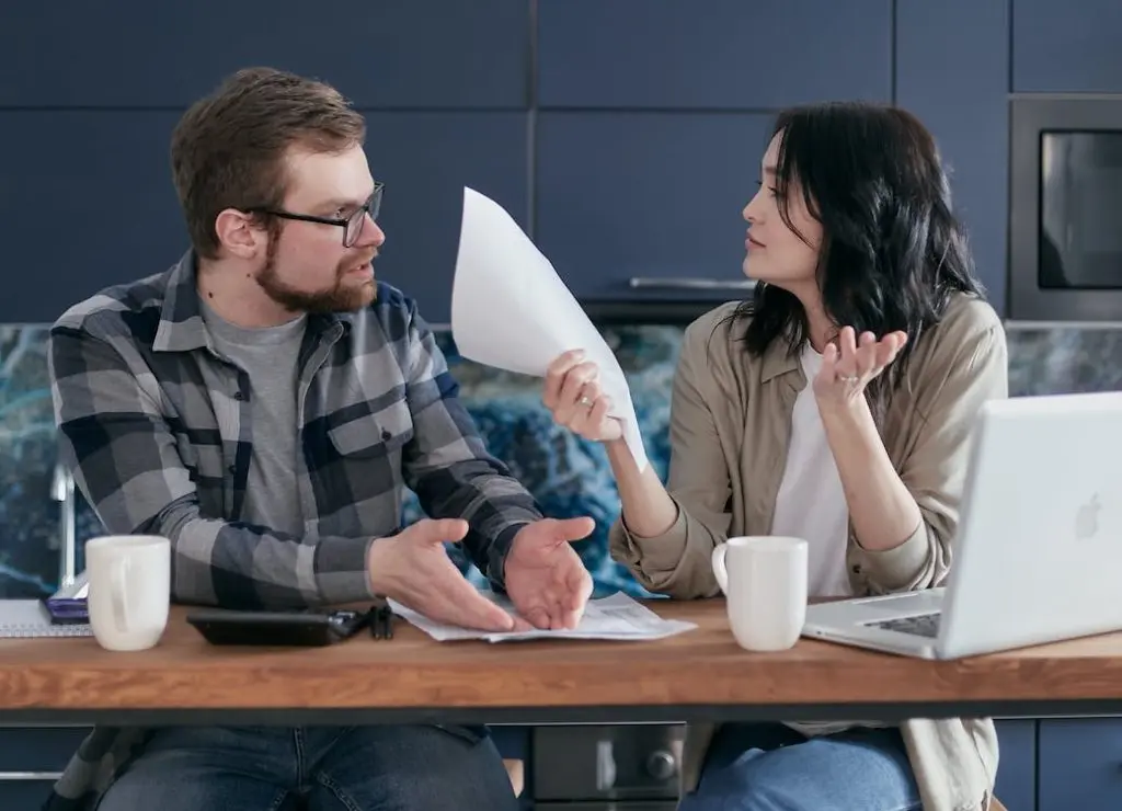 Trying to Sell a House after Filing a Divorce Frustrated couple arguing over paperwork at a kitchen table, representing the emotional and financial stress of selling a home during a divorce