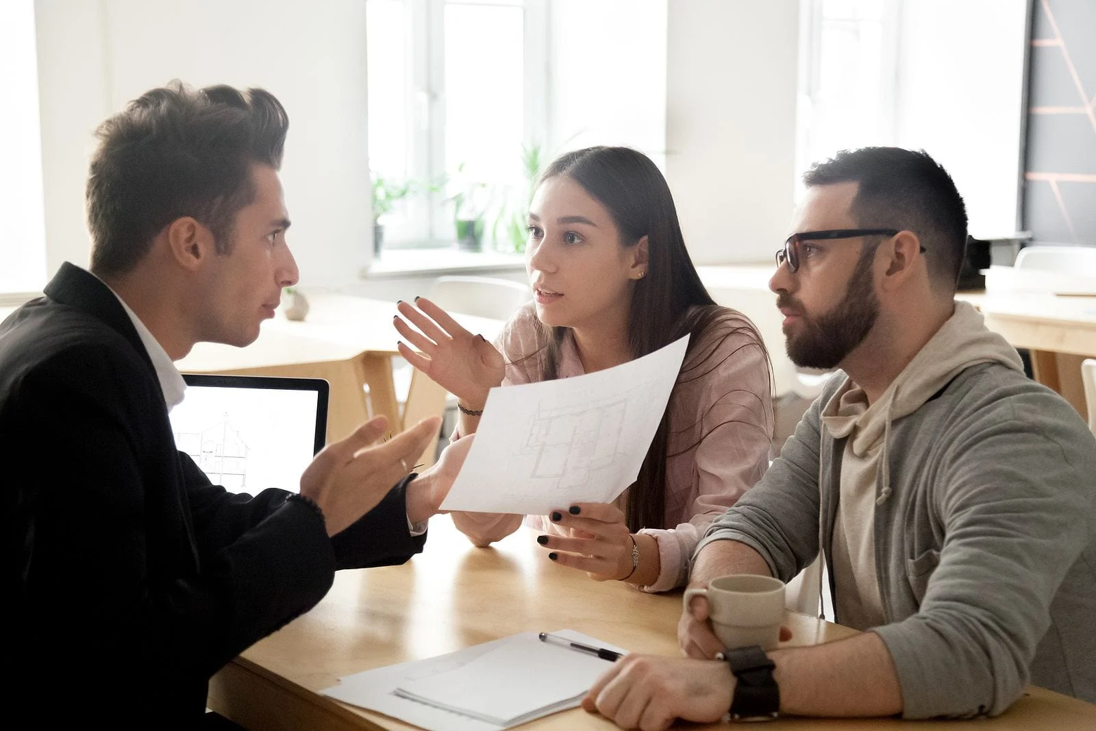 Landlord dealing with a frustrating tenant, trying to deescalate the situation, the landlord is across the desk from a couple having a stern conversation about their stay at his property