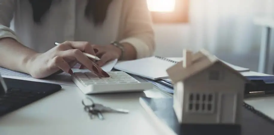 homeowner with a notepad and calculator with a photo of a model home signifying the tax benefits of seller financing