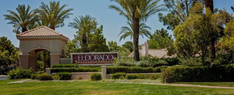 Entrance to the Eldorado neighborhood in North Las Vegas, Nevada, featuring lush landscaping, palm trees, and a welcoming neighborhood sign surrounded by greenery.