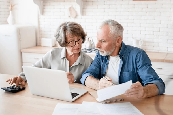 Senior couple reviewing reverse mortgage documents on a laptop while discussing options for selling their home and protecting heirs’ inheritance